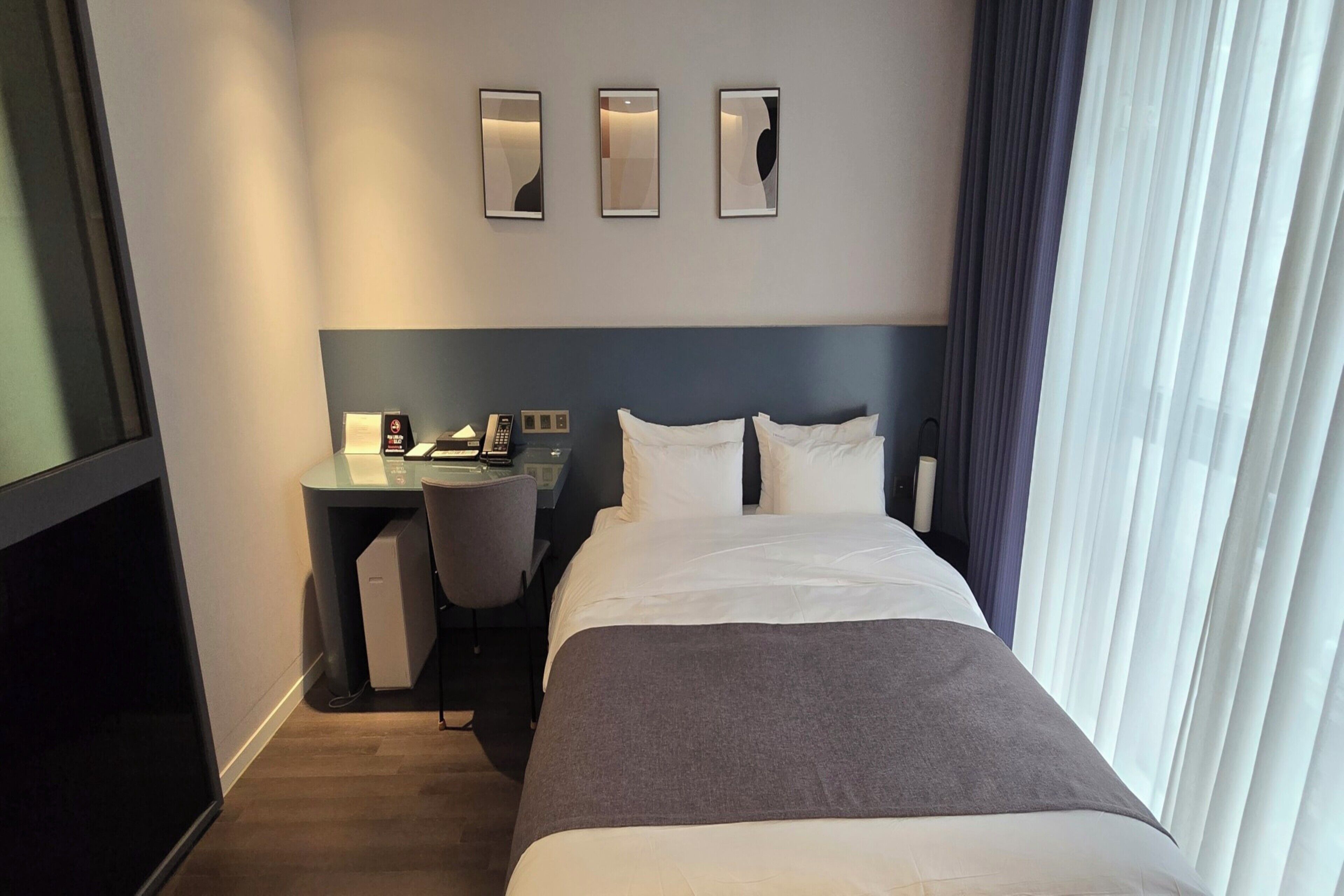 A hotel room with a bed, desk, chair, and three wall-mounted lights.