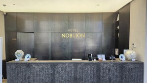 Una recepción con un mostrador oscuro y con textura, y una pared que muestra 'HOTEL NOBLION' en letras doradas.