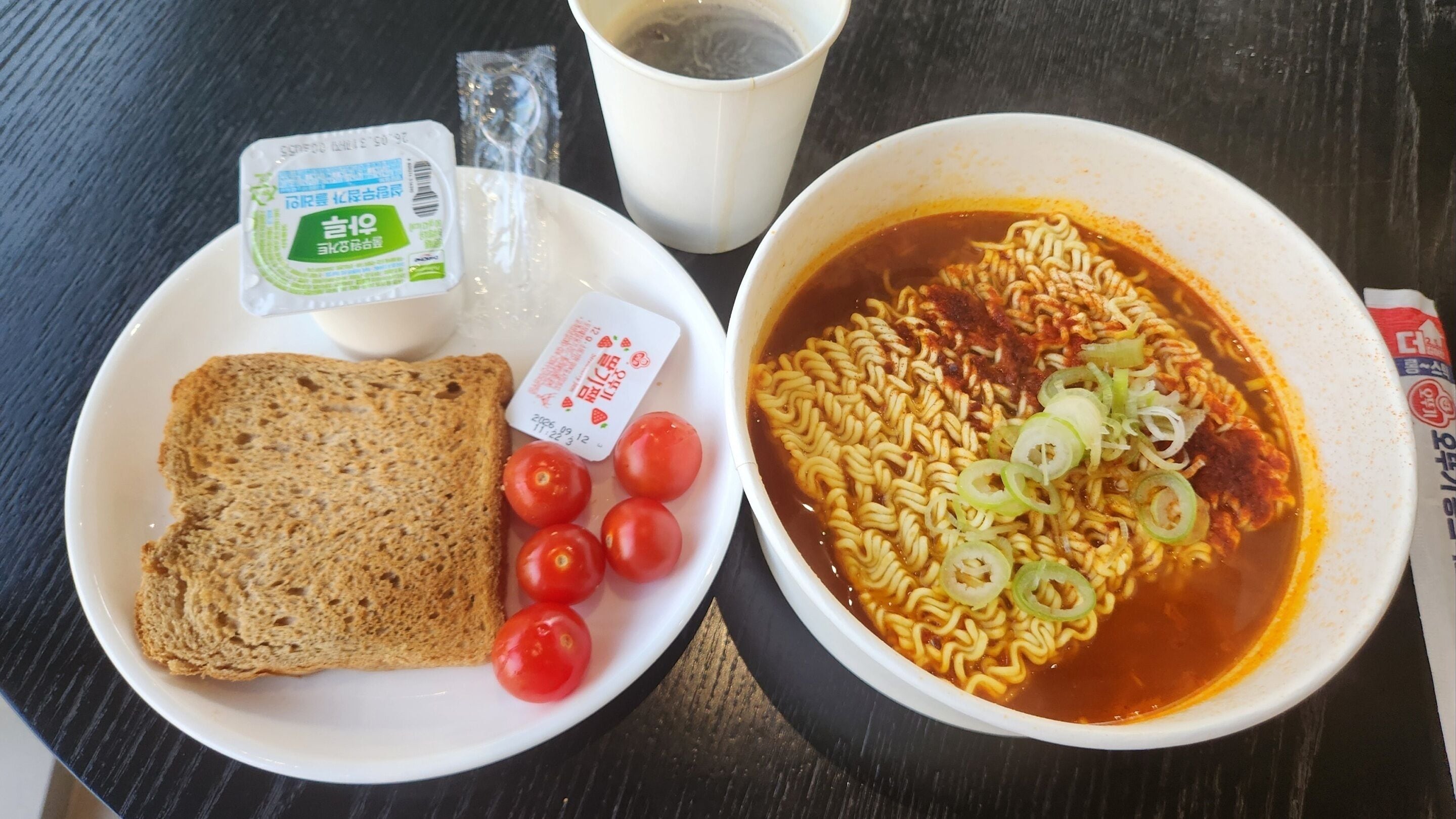 A meal with ramen, bread, and cherry tomatoes on a table.