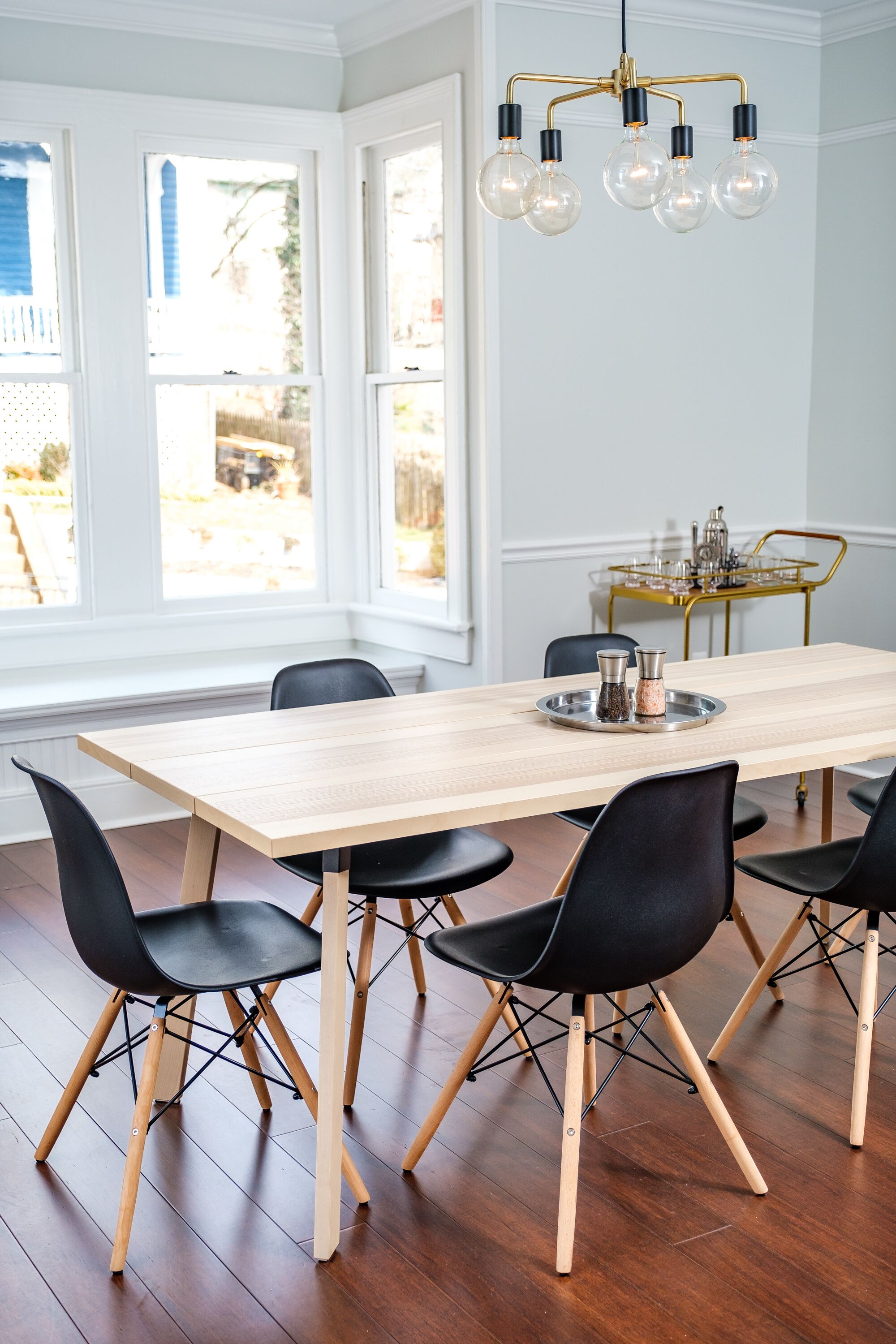 Un comedor con mesa de madera, sillas negras y una lámpara de araña.