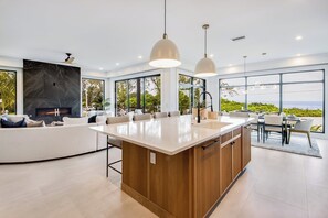 Una cocina moderna con una isla grande, electrodomésticos integrados y amplias ventanas con vistas al océano.