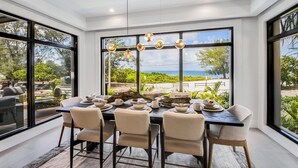 A dining area with a table set for six, large windows offering a view of the beach, and a modern chandelier. - Pier Pleasure - Anna Maria at it's finest! Pool, hot tub, beach, putting green (Anna Maria)