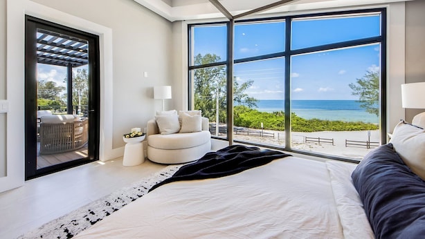 A bedroom with a large bed, a view of the ocean, a small seating area, and a balcony with outdoor furniture. - Pier Pleasure - Anna Maria at it's finest! Pool, hot tub, beach, putting green (Anna Maria)