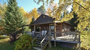 Een rustieke blokhut met een veranda, buitenzitplaatsen en een trap naar de ingang.