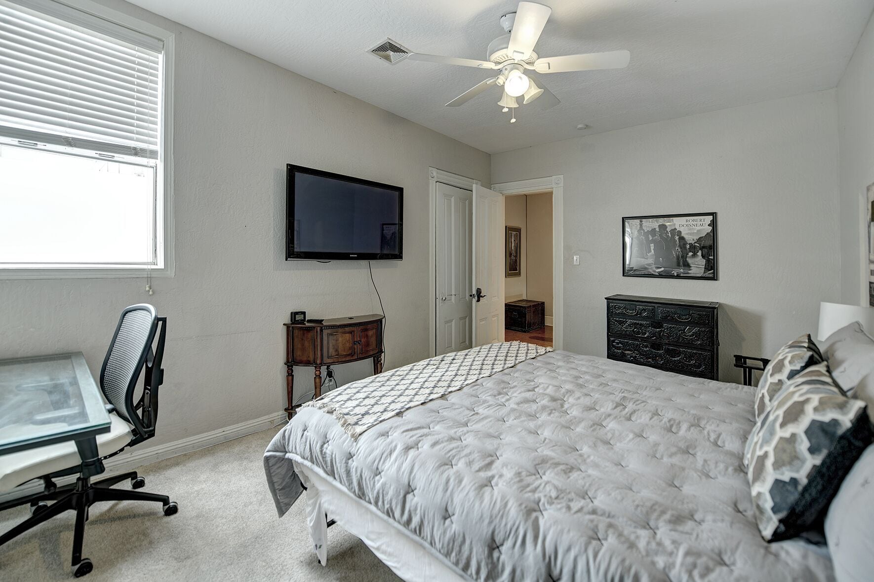 Une chambre à coucher comprenant un lit, un bureau, une chaise, une commode, un téléviseur et un ventilateur de plafond.