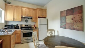 Una cocina con armarios de madera, estufa, refrigerador, microondas y una mesa de comedor con sillas.