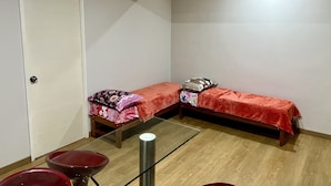A small, compact room with two single beds, a wooden table, and a glass-top table. - Acogedor Departamento en Lima - Jesús María, Ideal Para Familias (Jesús María)