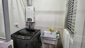 A compact bathroom with a washing machine, a sink, and a small window with blinds. - Acogedor Departamento en Lima - Jesús María, Ideal Para Familias (Jesús María)