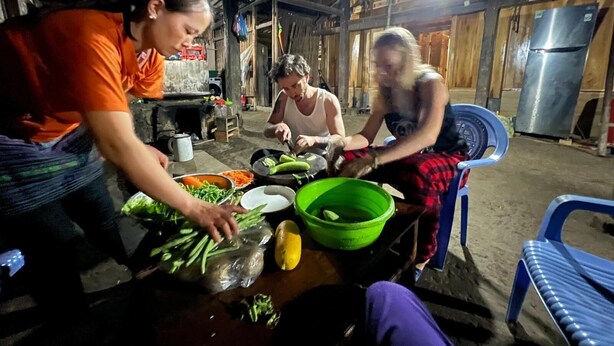 A rustic kitchen with a table filled with vegetables and a person preparing food. - Buffalo Eco House (Ta Van)