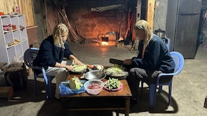 Two people preparing food at a wooden table with various vegetables and meat in a rustic room with a fireplace. - Buffalo Eco House (Ta Van)