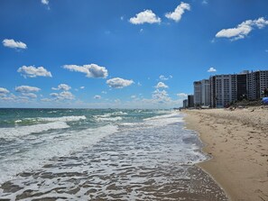 Ein Strand mit Wellen, einem klaren Himmel und hohen Gebäuden im Hintergrund.