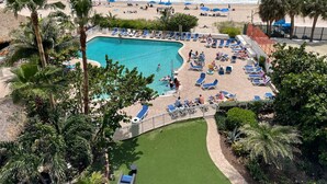 A pool area with lounge chairs and umbrellas, surrounded by palm trees and a view of the ocean. - Lovely  Partial Oceanview Condo at Ocean Manor Resort (Fort Lauderdale)