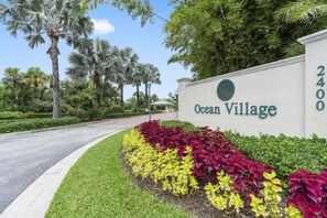Un cartel de Ocean Village, con una carretera que se curva a la izquierda y abundante vegetación.