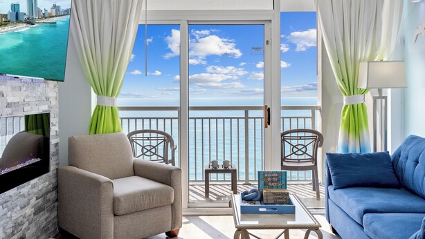 A balcony with a city view, a TV mounted on the wall, and two chairs. - 15th Floor Oceanfront Condo with Beach, 4 Pools, 2 Hot Tubs & a Lazy River (Myrtle Beach)