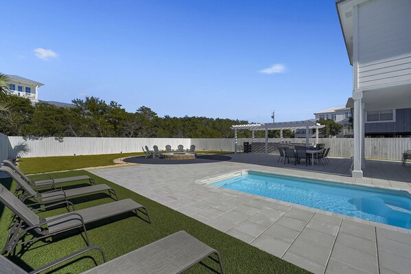 A backyard with a swimming pool, lounge chairs, a barbecue area, and a fenced yard.