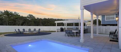 A backyard with a swimming pool, patio furniture, and a covered seating area.