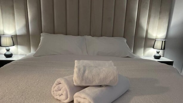 A neatly made bed with two rolled towels, a headboard, and two bedside lamps. - Hills Nomad Studio (București)
