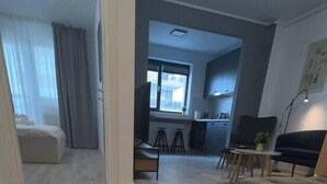 A modern living room with a sofa, a dining area with stools, a kitchen with cabinets, and a large window. - Hills Nomad Studio (București)