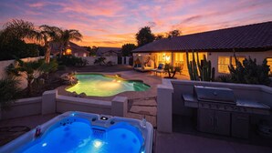 Un giardino sul retro con una vasca idromassaggio, un barbecue e una piscina al tramonto.