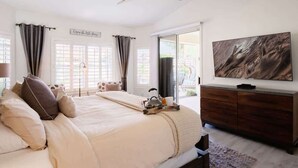 Una camera da letto con un letto, una televisione, un ventilatore a soffitto e una finestra con tende.