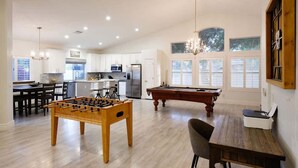 Un'ampia zona giorno con tavolo da calcio, tavolo da biliardo, tavolo da pranzo e angolo cottura completo di elettrodomestici.