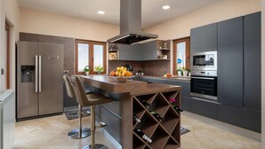 Una cocina moderna con una isla central, taburetes de bar, una estantería para vinos, horno empotrado y un refrigerador de acero inoxidable.