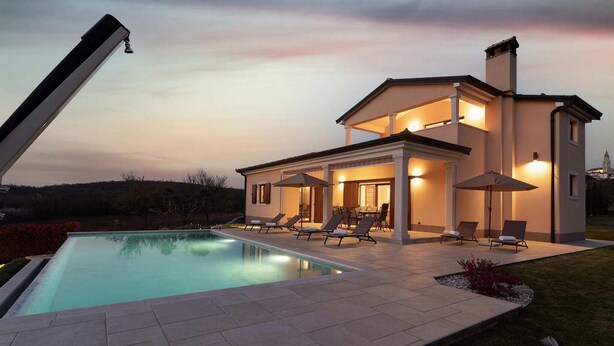 Una casa moderna de dos pisos con piscina, mobiliario exterior y un patio cubierto.