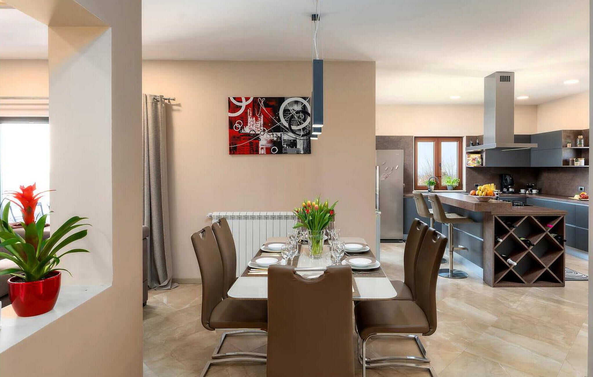 A modern dining area with a table set for four, a kitchen in the background, and a potted plant on the windowsill.
