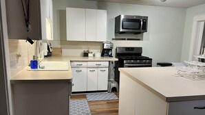 Une cuisine moderne avec des meubles blancs, un four à micro-ondes encastré, une cuisinière et une machine à café.