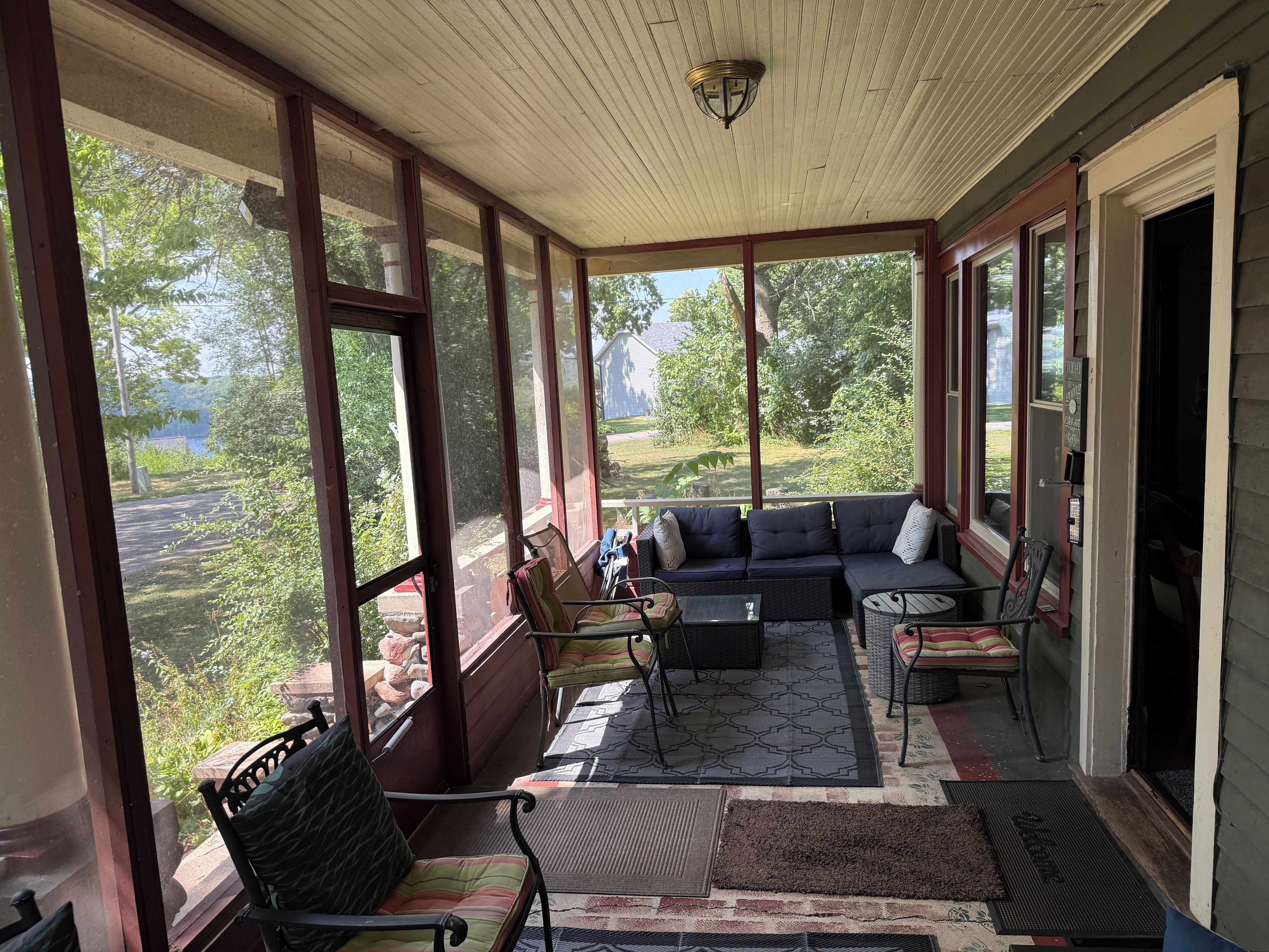 A covered porch with a sofa, chairs, and a table, overlooking a garden.