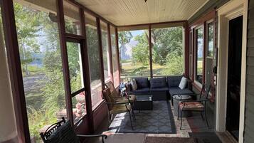 A covered porch with a sofa, chairs, and a table, overlooking a garden.