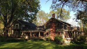 Une grande maison à deux étages, dotée d’une cheminée en briques, d’un porche abrité et d’une pelouse bien entretenue.