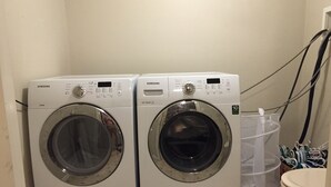 Deux lave-linge à chargement frontal Samsung blancs, dans une petite buanderie dont le sol est carrelé.