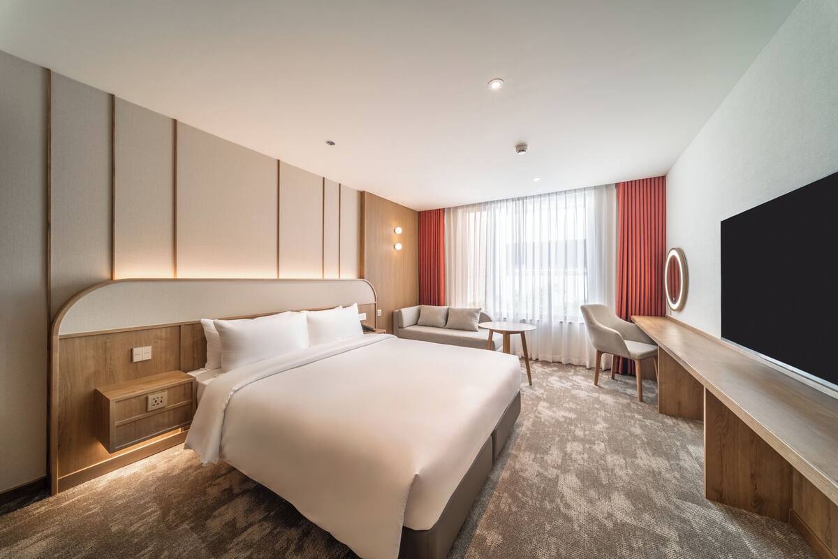 Ein Hotelzimmer mit einem großen Bett, einem Schreibtisch, einem Sessel und einem Fernseher.