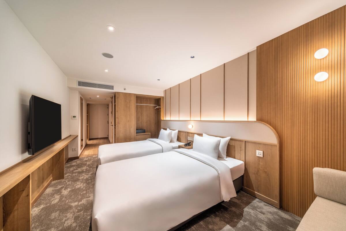Ein Hotelzimmer mit zwei Betten, einem Fernseher, Holzvertäfelung und einem begehbaren Kleiderschrank.