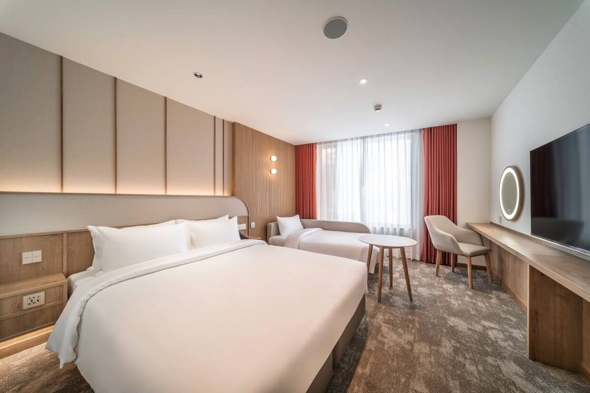 Ein Hotelzimmer mit zwei Betten, einem Schreibtisch, einem Stuhl, einem Fernseher und einem Fenster mit Vorhängen.