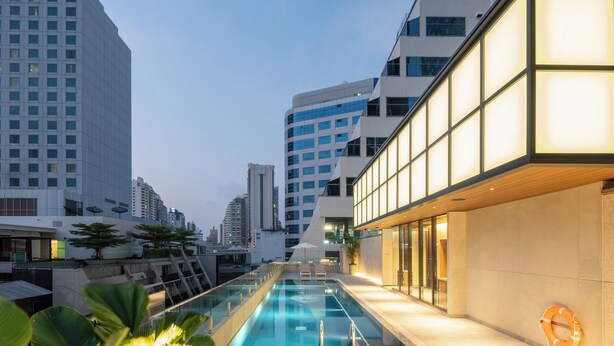 Une piscine sur le toit, délimitée par une paroi en verre, entourée de bâtiments modernes et surplombant un ciel dégagé.