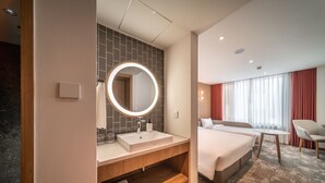 Une chambre d’hôtel moderne, dotée d’un grand miroir rond, d’un lavabo, d’une coiffeuse, d’un lit, d’un bureau et d’une chaise.