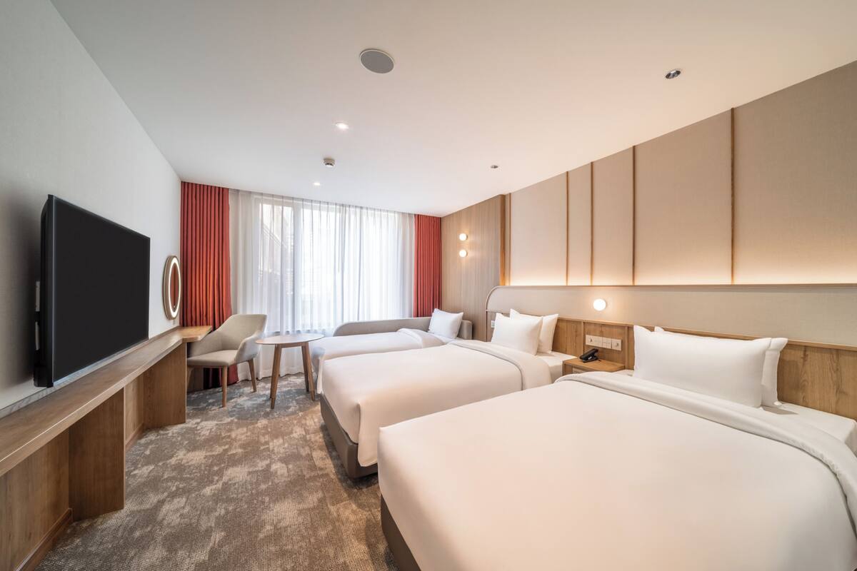 Ein Hotelzimmer mit zwei Betten, einem Schreibtisch, einem Flachbildfernseher, einem kleinen Tisch und einem Stuhl.