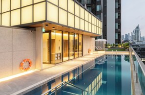 Ein modernes Hotel mit einem gläsernen Poolbereich, einem Rettungsring an der Wand und einer Stadtansicht im Hintergrund.