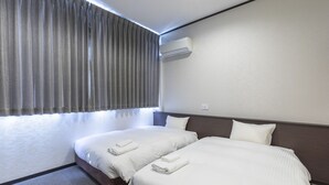 A hotel room with two beds, a window with curtains, an air conditioning unit, and a textured wall. - OSAKA PORT HOTEL L'ESPOIR (Osaka)