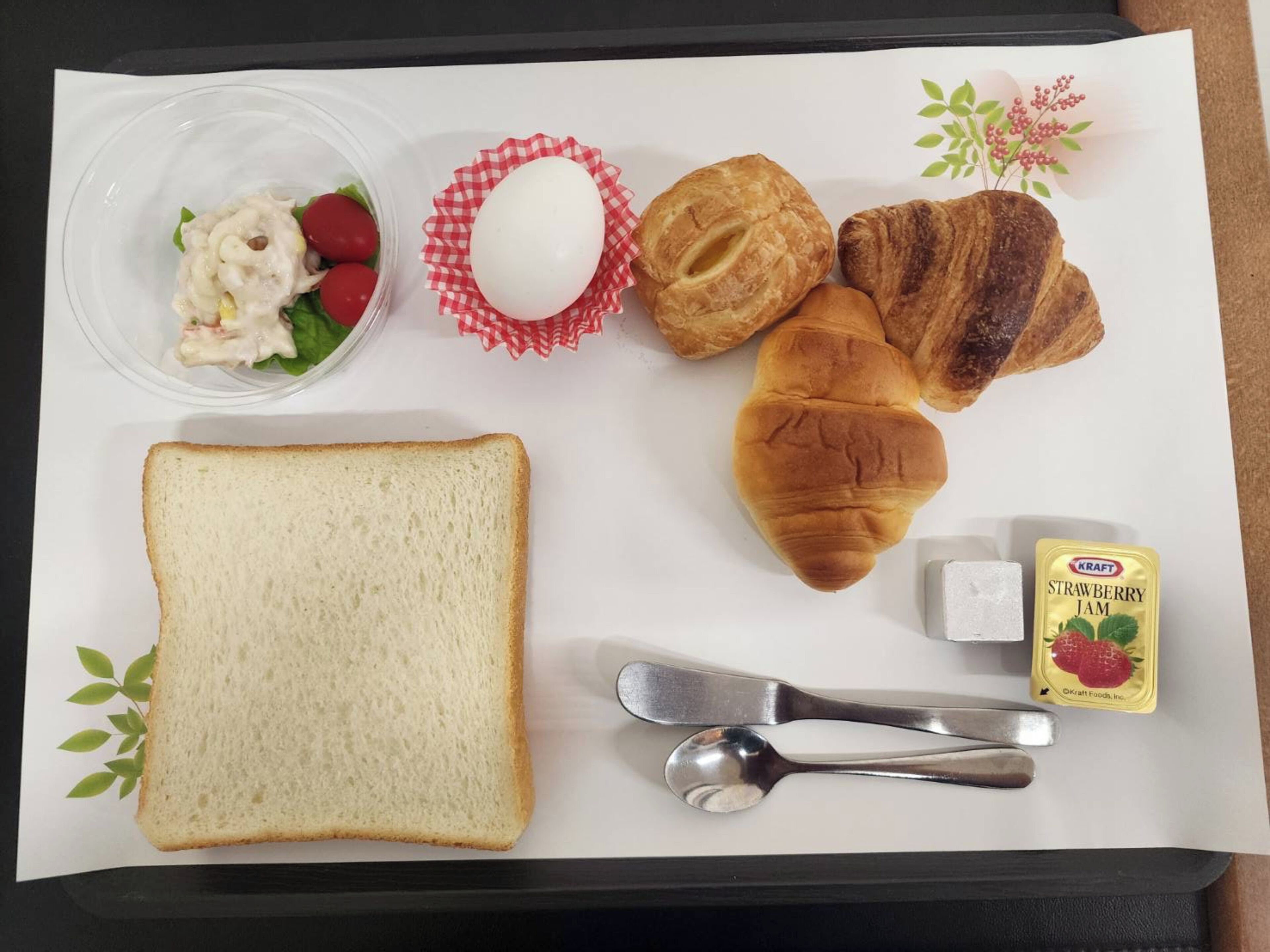 Egy tálca, rajta szendvics, croissantok, egy főtt tojás, egy saláta és egy üveg eperlekvár.