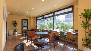 A modern indoor seating area with a round table and chairs, large windows with a view of the city, and potted plants. - OSAKA PORT HOTEL L'ESPOIR (Osaka)
