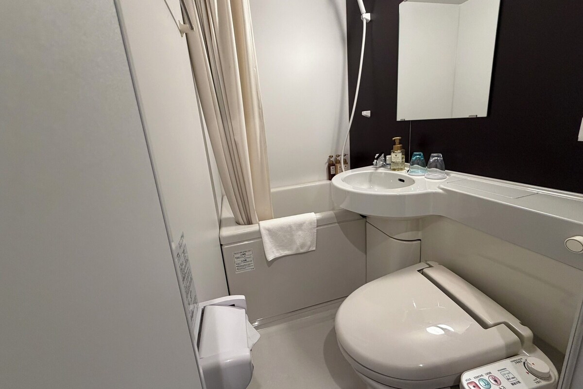 A modern bathroom with a white toilet, a sink with toiletries, a shower, and a mirror.