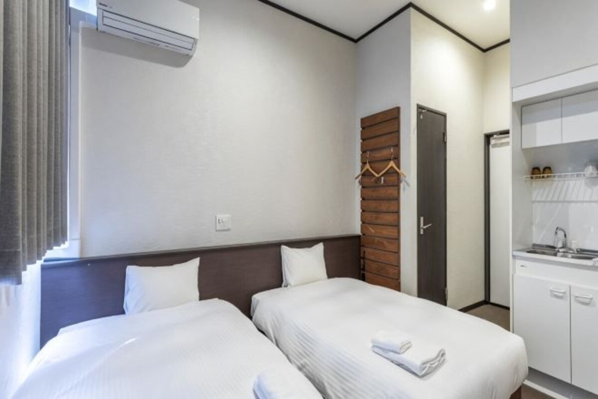 A hotel room with two beds, a wooden headboard, a kitchenette, and a wardrobe.