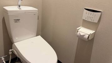 Sanitário com caixa de descarga TOTO, dispensador de toalhas de papel e dispensador de álcool em gel.