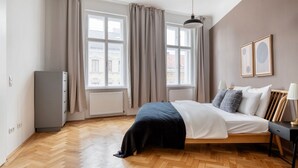 A bedroom with a bed, a dresser, a radiator, and two windows with curtains. - Tasteful Margareten 1BR, Fully Furnished & Equipped, by Blueground (Vienna)