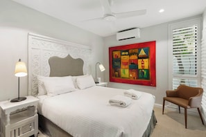 A hotel room with a bed, a chair, a painting, and a ceiling fan.