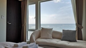 A hotel room with a large window offering a view of the sea, a sofa with pillows, and neatly folded towels on the bed. - Otaru Geihinkan (Otaru)