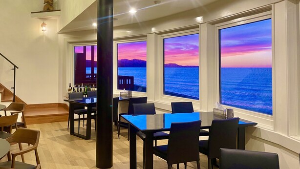 A dining area with a view of the ocean through large windows, a bar area with bottles, and a staircase leading to an upper level. - Otaru Geihinkan (Otaru)